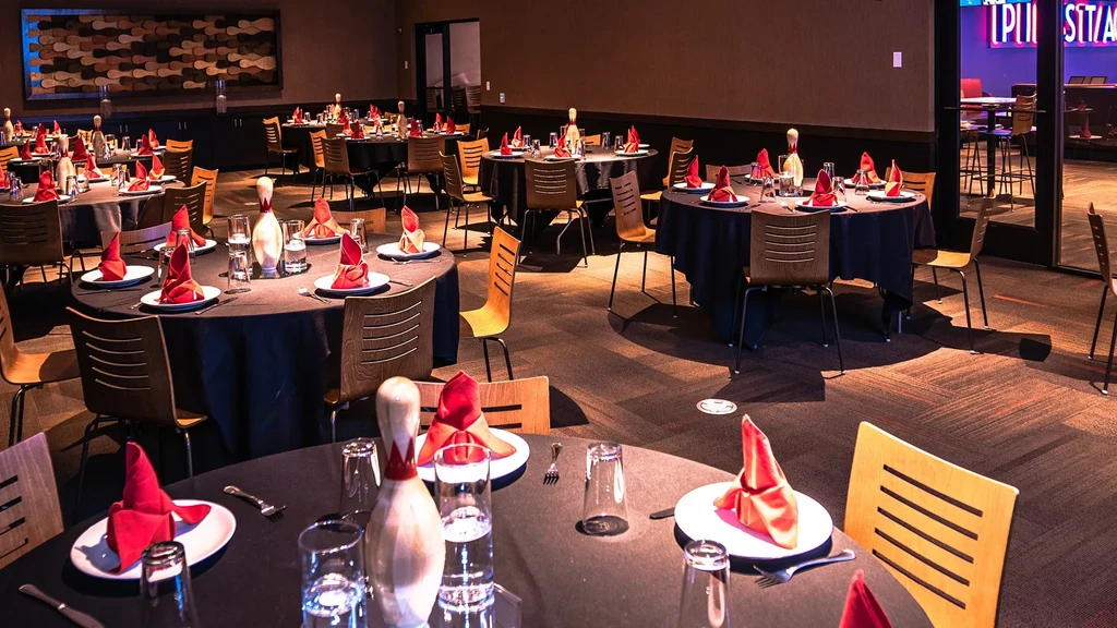 Themed banquet hall with tables, bowling pins, and neon signs.