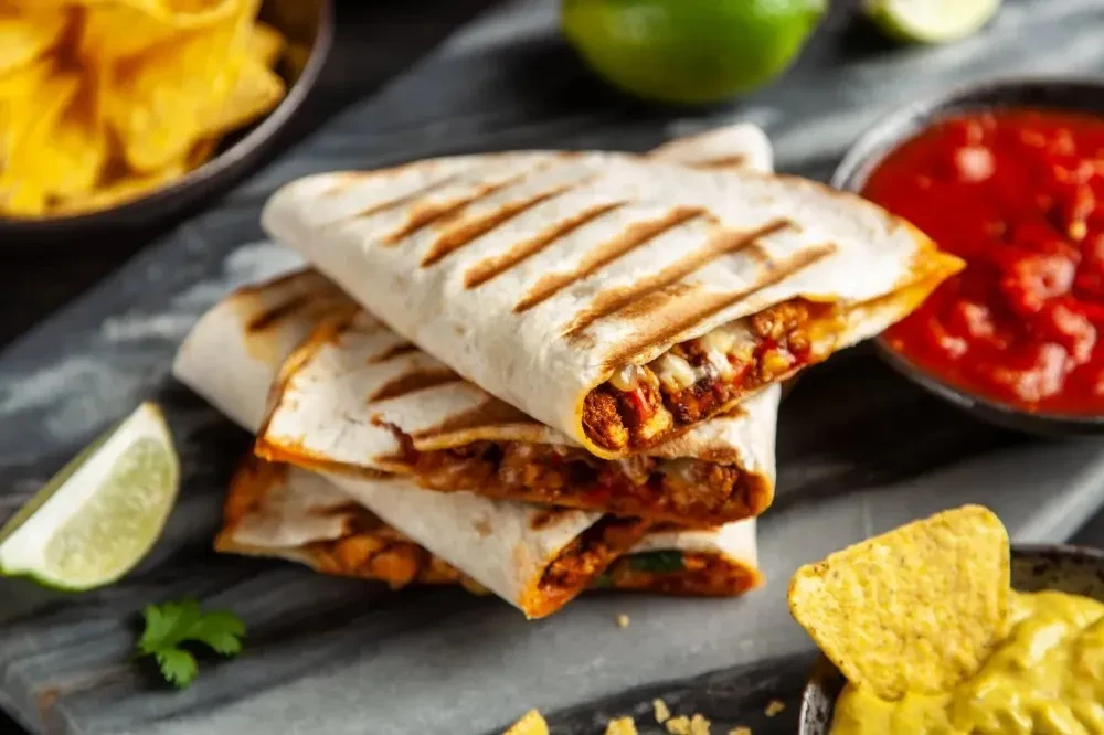 Grill-marked quesadilla wedges with meat, cheese, lime, salsa, chips.