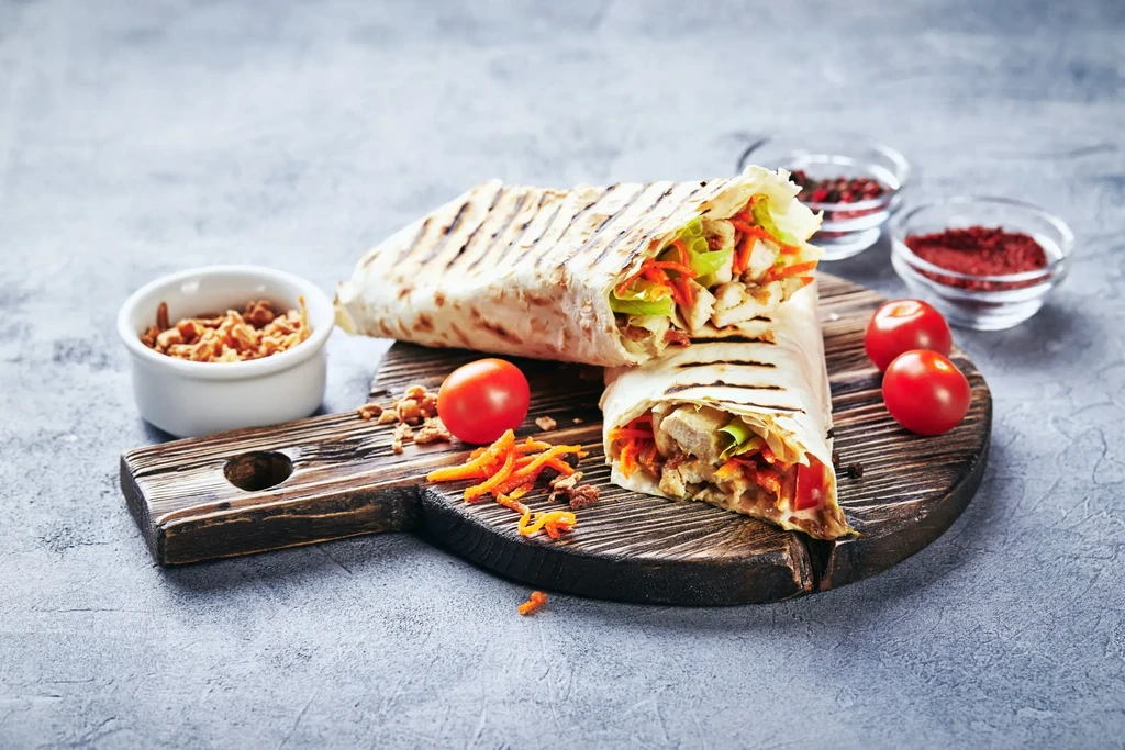Grilled chicken wrap halves with vegetables and spices on wooden board.