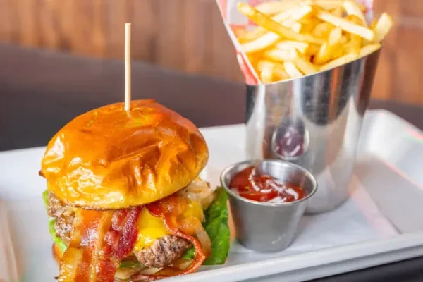 Burger with melted cheese, bacon, fries, and ketchup.