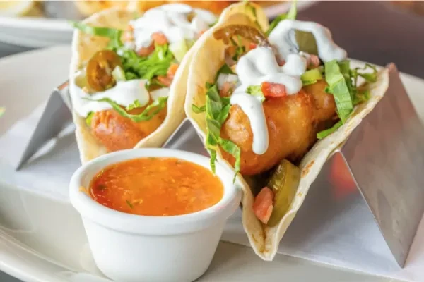 Two tacos with crispy fried filling, lettuce, tomatoes, and orange sauce.