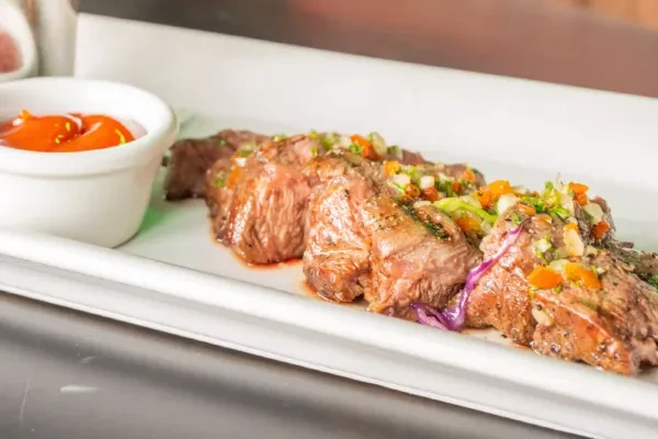Slices of cooked meat with colorful relish and a side of orange sauce.
