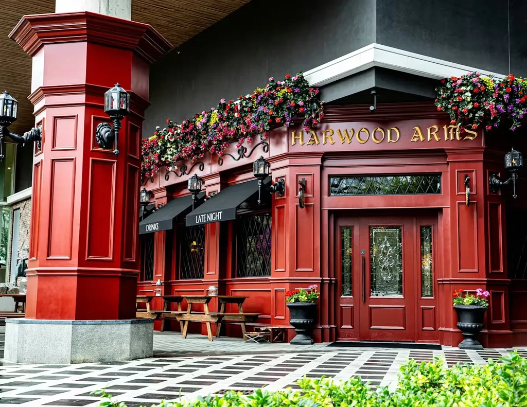 Harwood Arms pub exterior with paneled walls, vibrant flowers, outdoor seating.