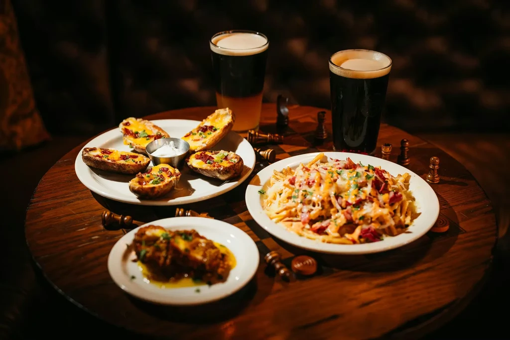 Loaded potato skins, fries, chicken, and dark beers with chess pieces.