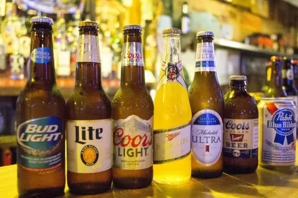 Lineup of various cold beer bottles and one can on a bar.
