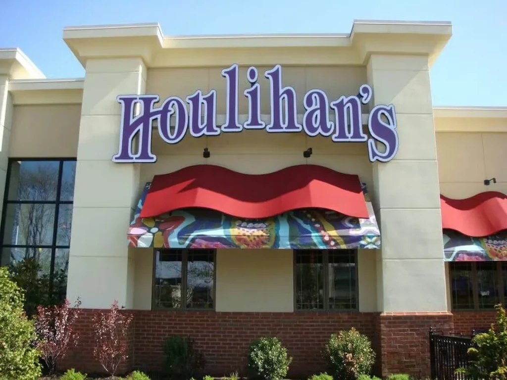 Exterior of Houlihan's restaurant with purple sign and red awnings on sunny day.