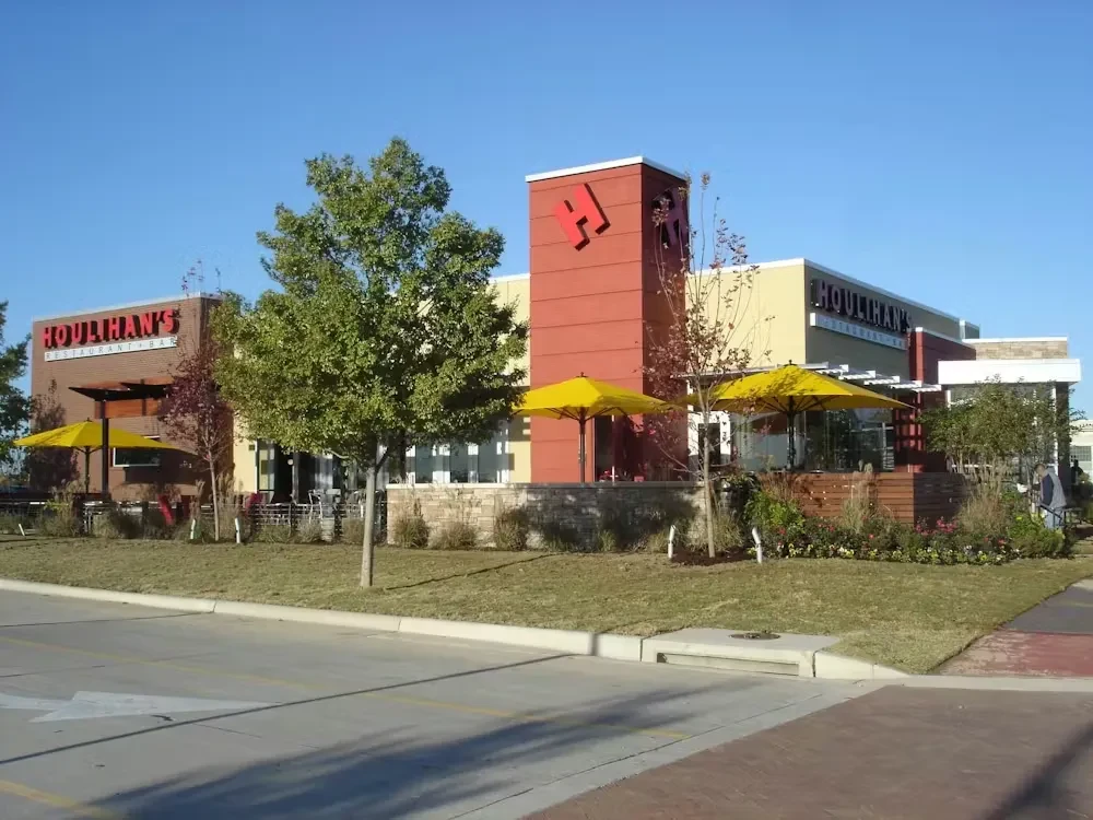 Sunny Houlihan's restaurant exterior with patios, yellow umbrellas, and landscaping.