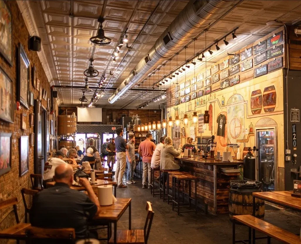 Rustic industrial restaurant interior with a long bar, mural, and patrons.