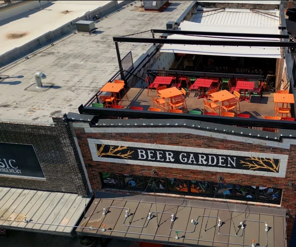 High-angle urban rooftop beer garden with colorful tables and 'BEER GARDEN' sign.
