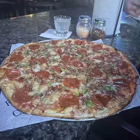 Large pizza with pepperoni, sausage, and bell peppers on a dark counter.