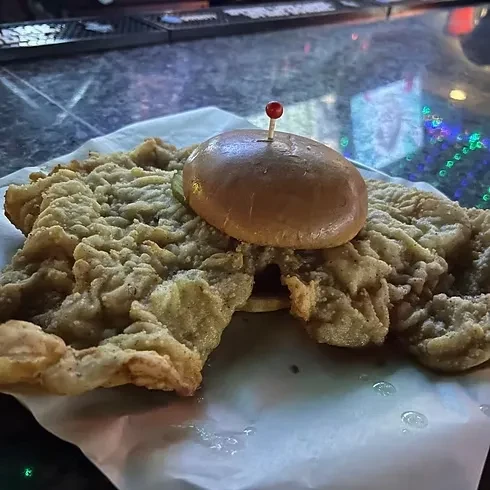 Large fried sandwich with bun and toothpick in a dim restaurant.