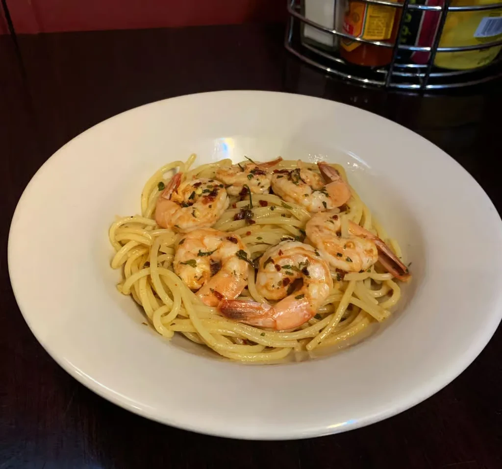 White bowl of shrimp pasta topped with chili flakes and herbs.