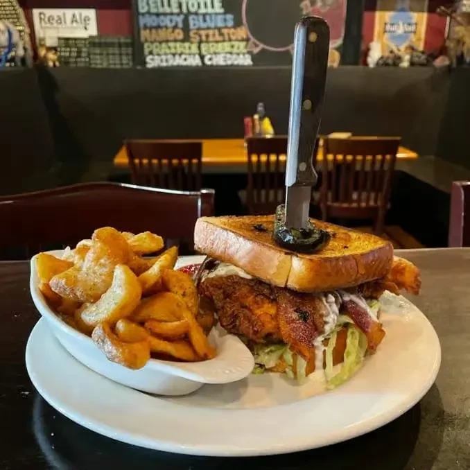 Crispy fried chicken sandwich, wedge fries on plate, restaurant background.