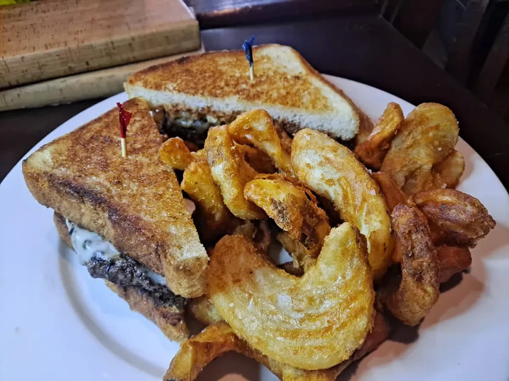 Grilled sandwich with meat, melted cheese, and crispy potato wedges.