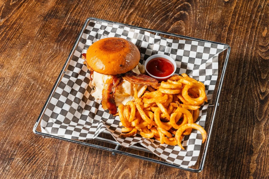 Top-down: burger, curly fries, and ketchup in a checkered basket.