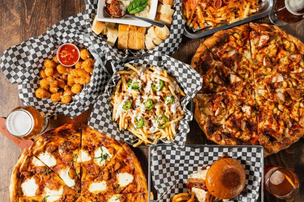 Overhead spread of pizza, fries, burger, and drinks on a wooden table.