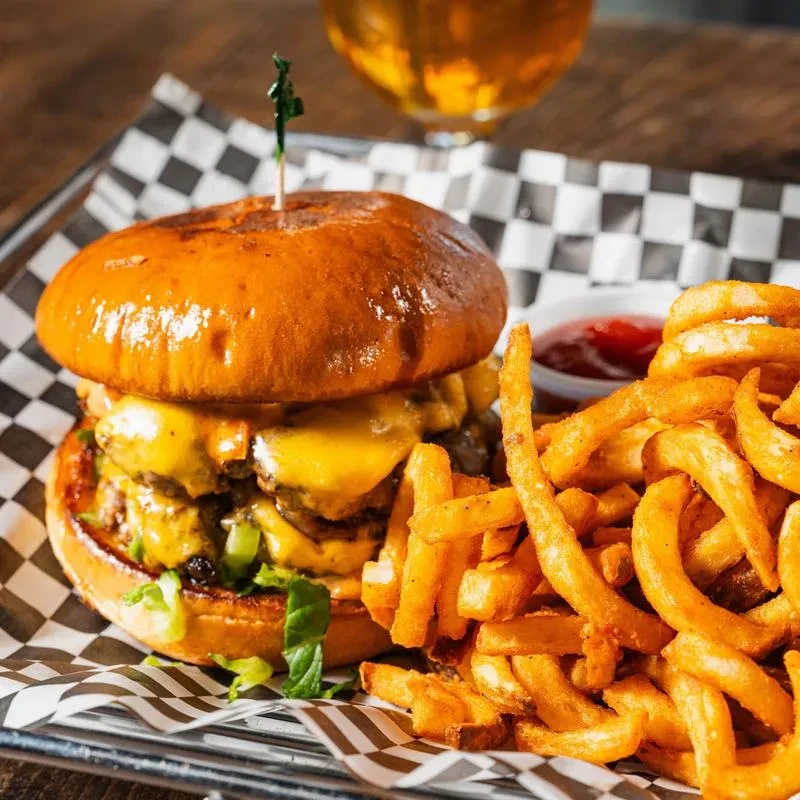 Close-up of a double cheeseburger, curly fries, and ketchup.