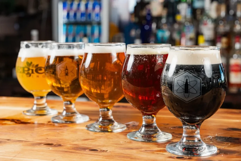 Five tulip glasses of diverse beers on a wooden bar top.