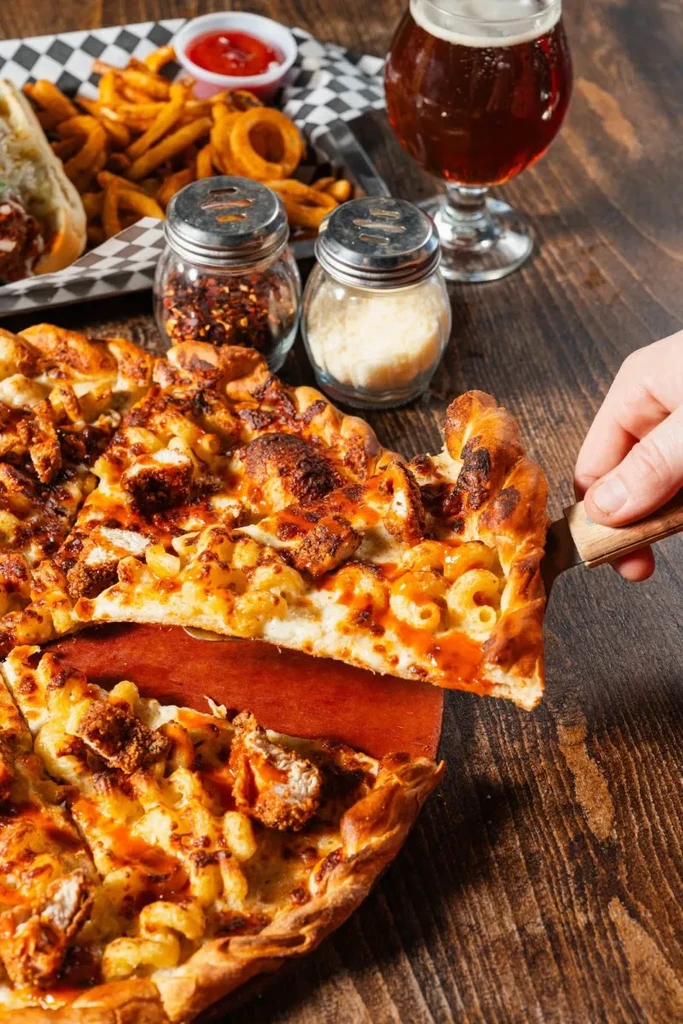 Hand lifting mac and cheese fried chicken pizza slice with fries, beer.