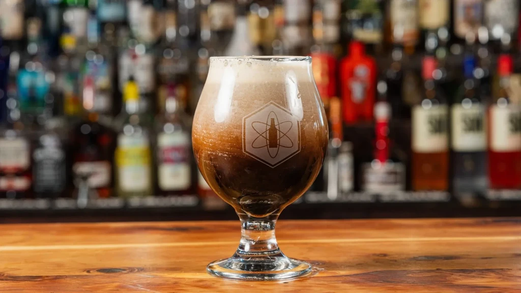 Dark, foamy beer in a logo-etched stemmed glass on a wooden bar.
