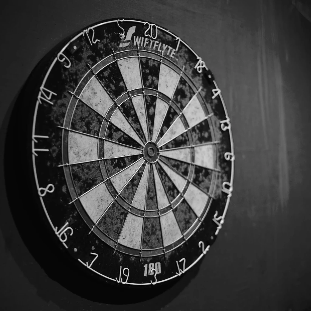 Worn WIFTFLYTE dartboard in black and white mounted on a dark wall.