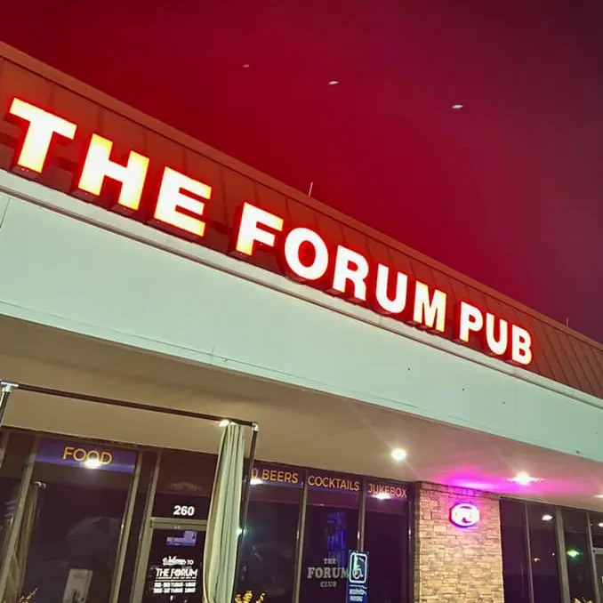The Forum Pub exterior at night with bright red illuminated sign.