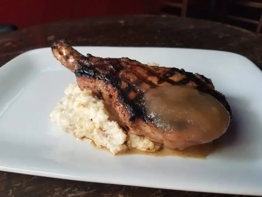 Grilled bone-in pork chop with sauce and mashed potatoes.