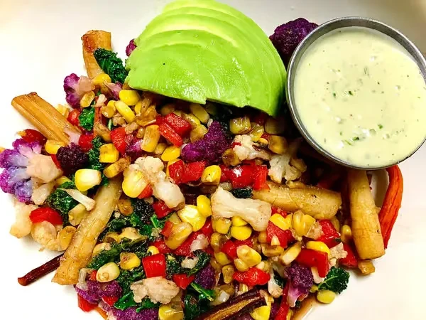 Vibrant cooked vegetables and grains with avocado and green sauce.