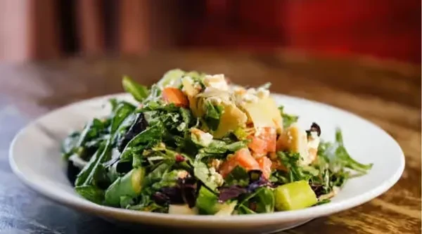 Close-up of a fresh salad with greens, tomatoes, avocado, and crumbled cheese.