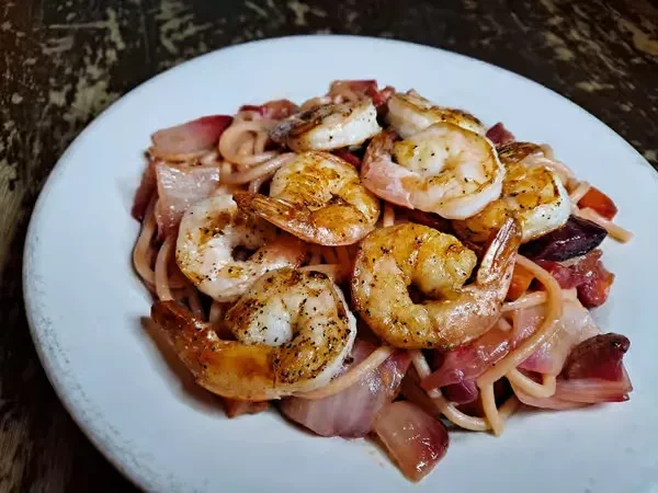 Close-up of pasta, grilled shrimp, and sautéed red onions.