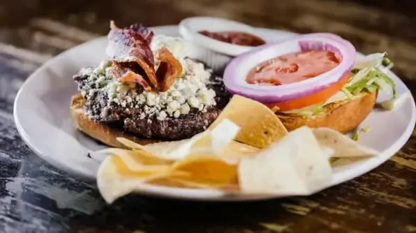 Deconstructed gourmet burger with blue cheese, bacon, lettuce, tomato, and chips.