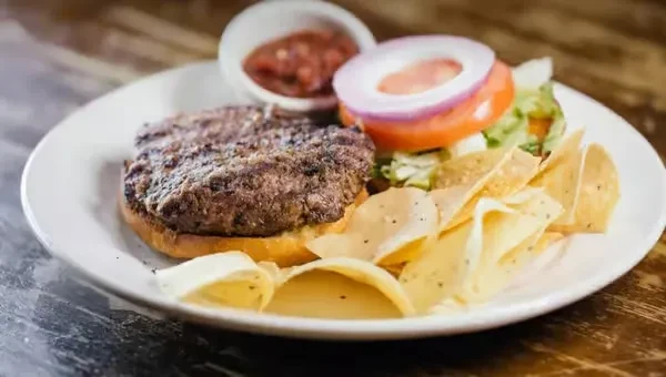 Open-faced burger with chips, salsa, lettuce, tomato, and onion.