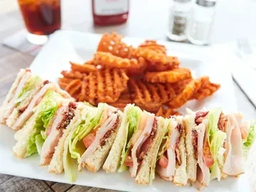 Toasted club sandwich with bacon, lettuce, tomato, and waffle fries.