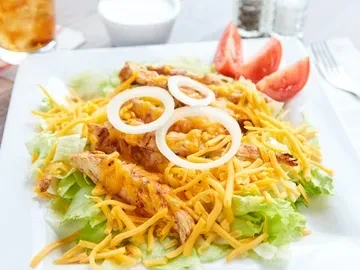 Salad with lettuce, shredded chicken, cheese, onion rings, and tomato wedges.