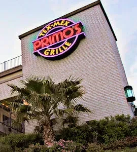 Tex-Mex Primo's Grille, a brick building with bright neon sign at dusk.