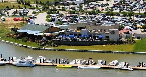 Waterfront restaurant complex with blue umbrellas, boats, and full parking lot.