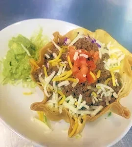 Taco salad in a crispy tortilla bowl with ground beef and guacamole.