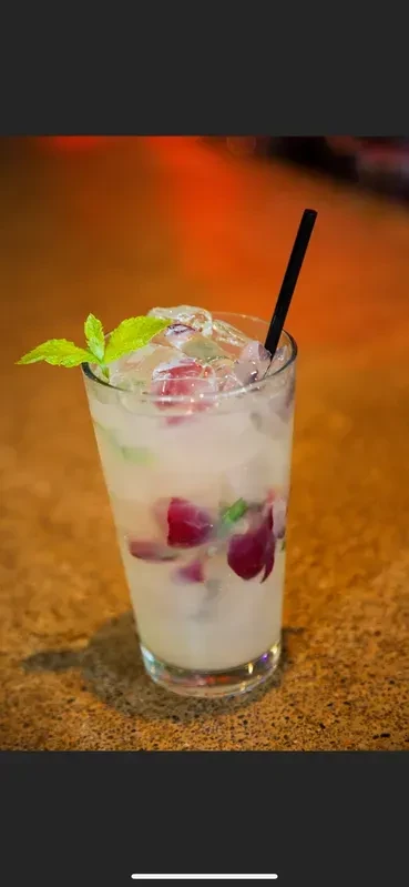 Glass of milky drink with ice, mint, and reddish-purple fruit.