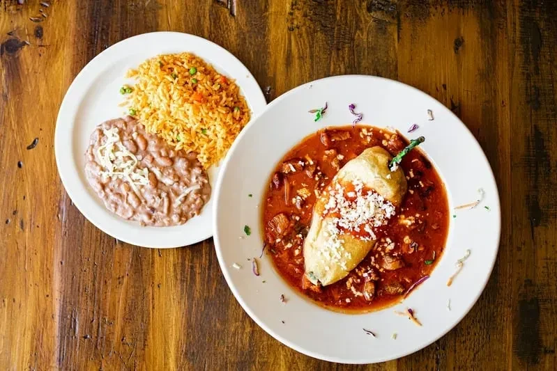Two plates of cheesy rice, refried beans, and a saucy chili relleno.