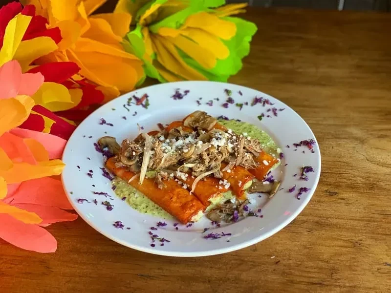 Plate of sauced rolled tortillas with shredded meat, cheese, and green drizzle.