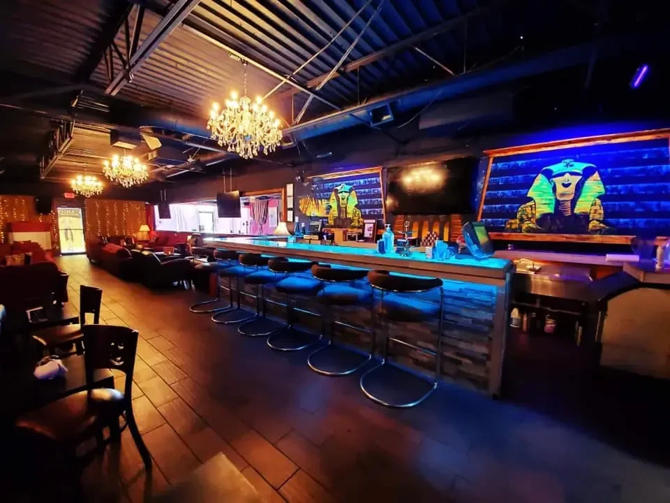 Bar interior with blue LED counter, pharaoh murals, chandeliers, and seating.