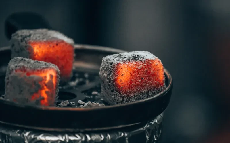 Three glowing red charcoal cubes and ash on a metal grate.