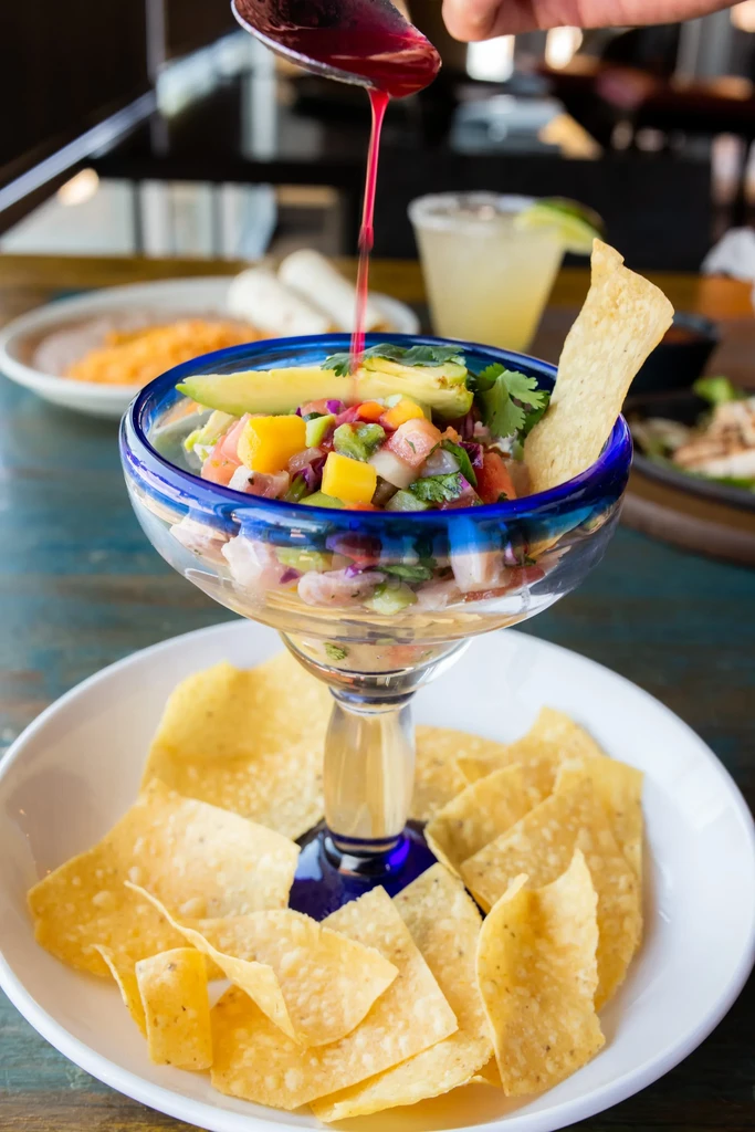 Ceviche in a margarita glass, surrounded by chips, sauce poured.