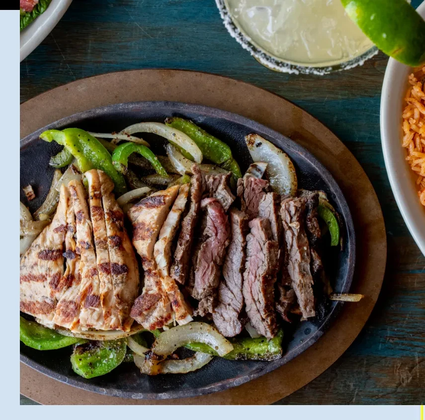 Sizzling chicken and steak fajitas with peppers, onions, margarita, and rice.