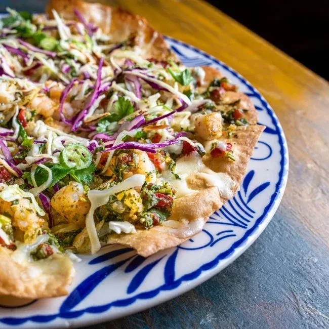 Top-down, vibrant shrimp flatbread with cheese, cabbage, and salsa.