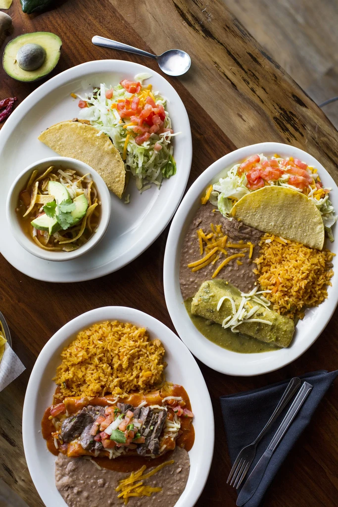 Overhead view of three plates of Mexican dishes on a wooden table.