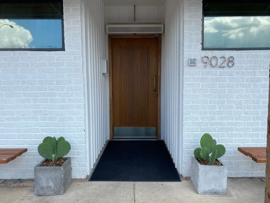 Modern white brick building entrance with wooden door, cacti, and 9028.