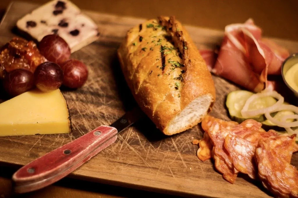 Rustic charcuterie board with cheese, bread, ham, grapes, and spreads.