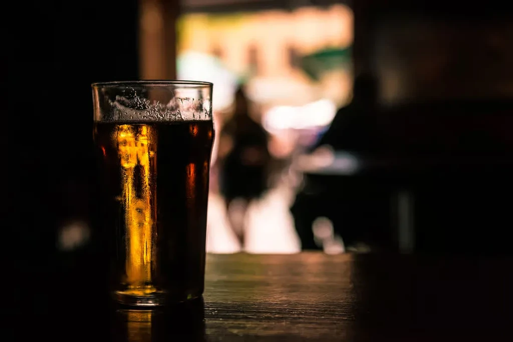 Condensed glass of amber liquid on a dark reflective wooden table.