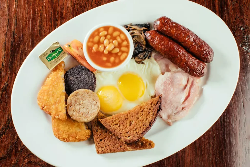 Full breakfast on oval plate: eggs, bacon, sausages, beans, toast.